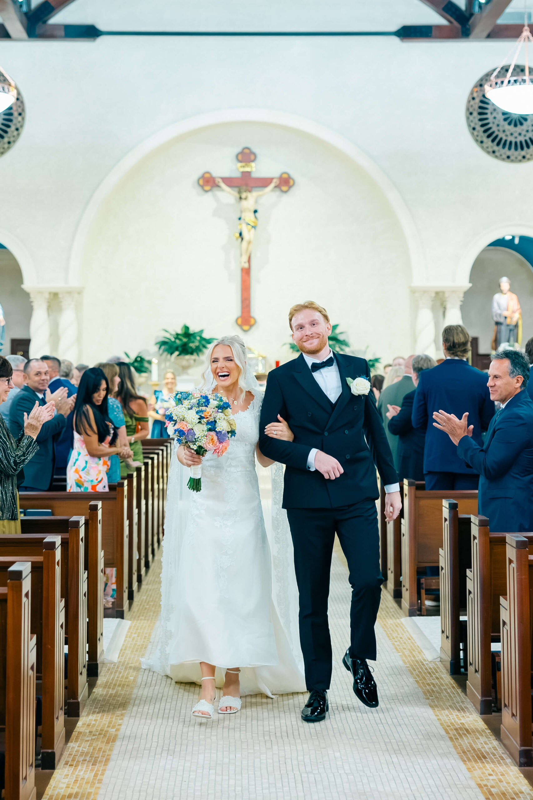 Just married Catholic bride and groom walking down the aisle with a crucifix in the background.